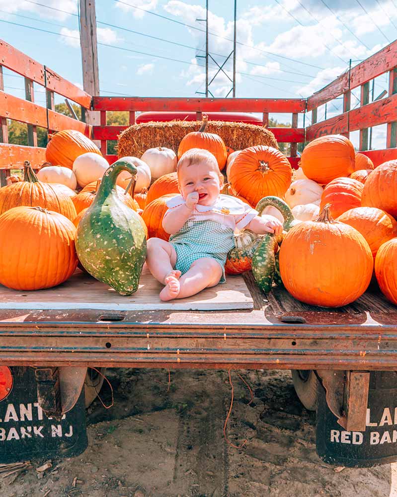 Baby sucking thumb in pumpkin truck