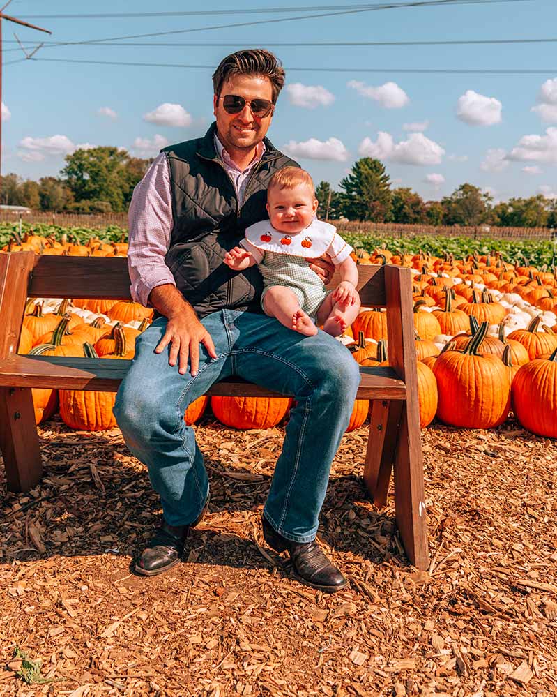 Man and Baby sitting on bench in front of pumpkin patch