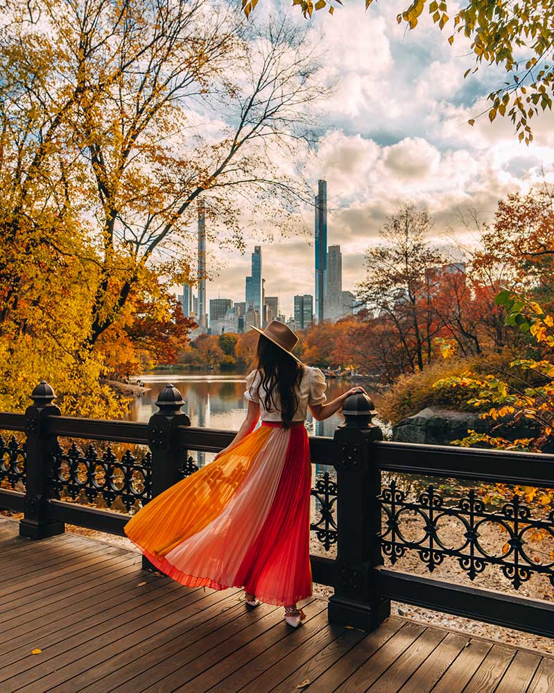 Kristi Hemric (Instagram: @khemric) poses on the Oak Bridge in Central Park surrounded by fall foliage and the NYC skyline