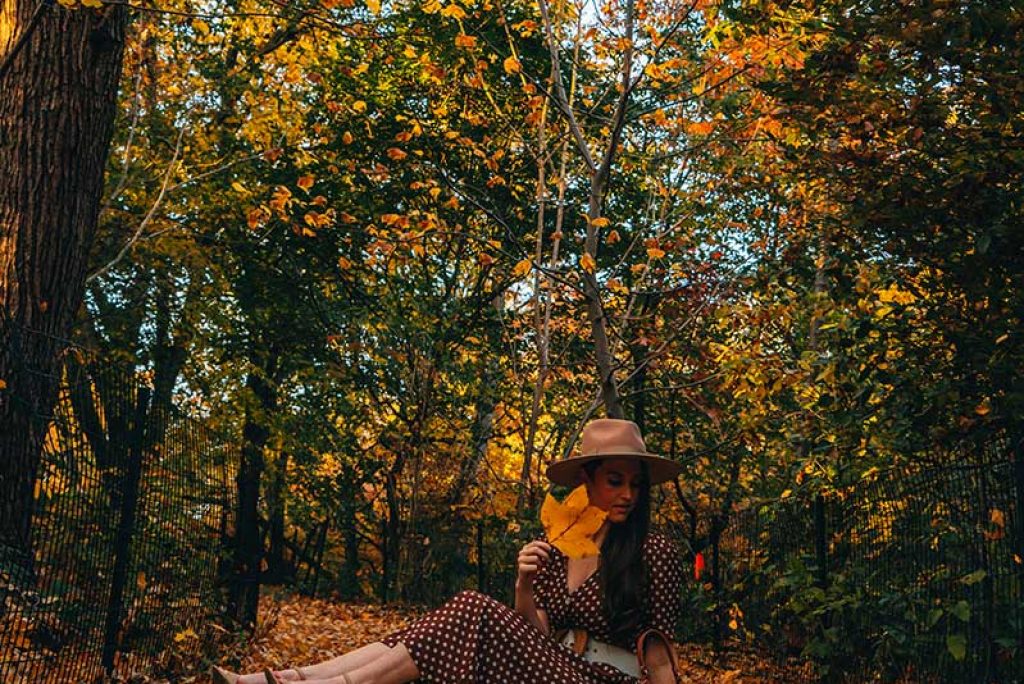 Kristi Hemric (Instagram: @khemric) sitting in The Ramble at Central park surrounded by autumn foliage